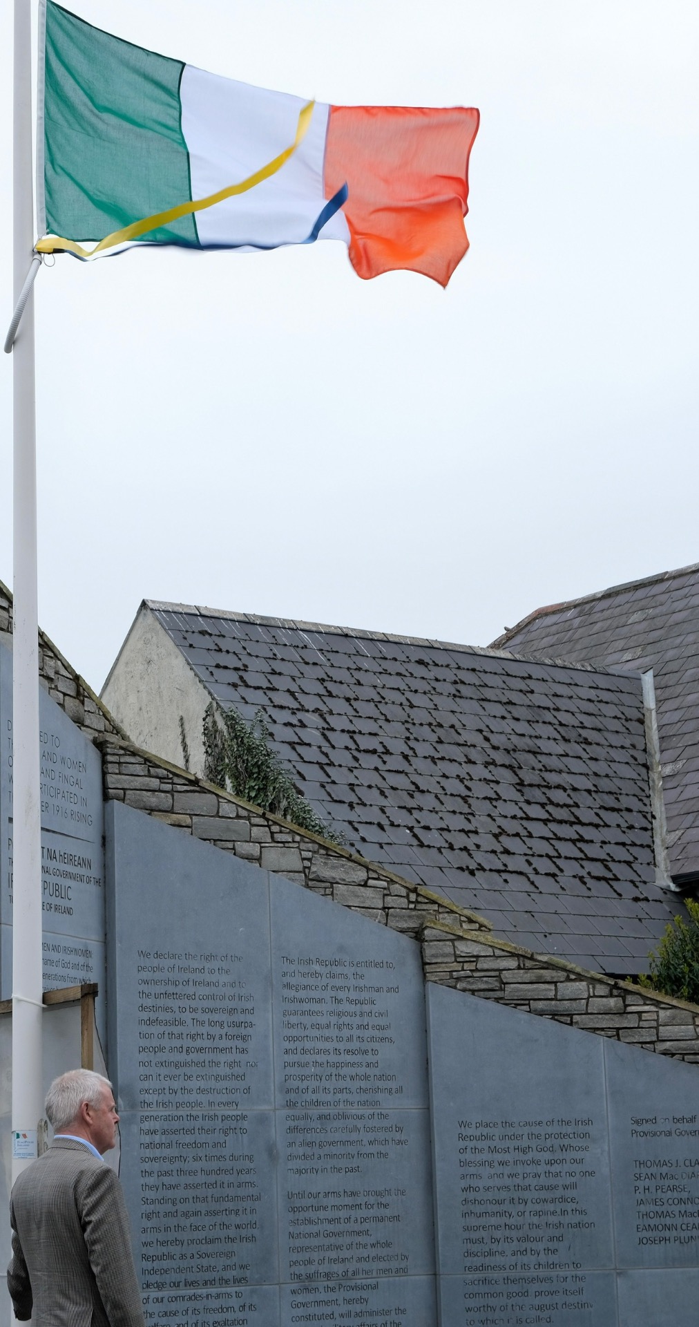 Green-white-red tricolor flag flutters above solar-paneled building, with stone walls and text panels below.